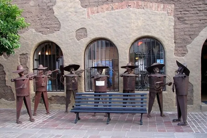 Metal sculptures of a mariachi band playing instruments near a bench